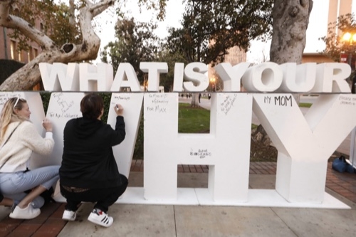 Two people writing on a sign that says "What is your why?"